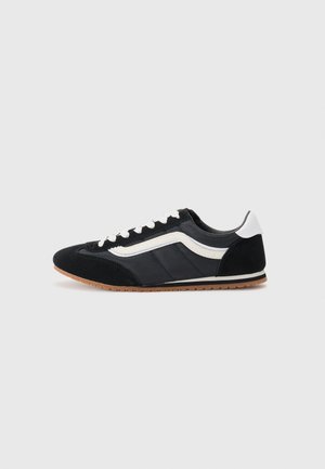 Schwarzer Sportschuh mit Obermaterial aus Wildleder und Textil, weißen Akzenten, sechs Ösen und Gummisohle. Schlanker Schnitt mit niedrigem Profil.