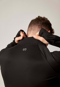 Schwarzer athletischer Pullover mit hohem Kragen, glatter Textur und einem kleinen Logo auf der Rückseite. Die Ärmel sind eng anliegend und bedecken die Handgelenke.