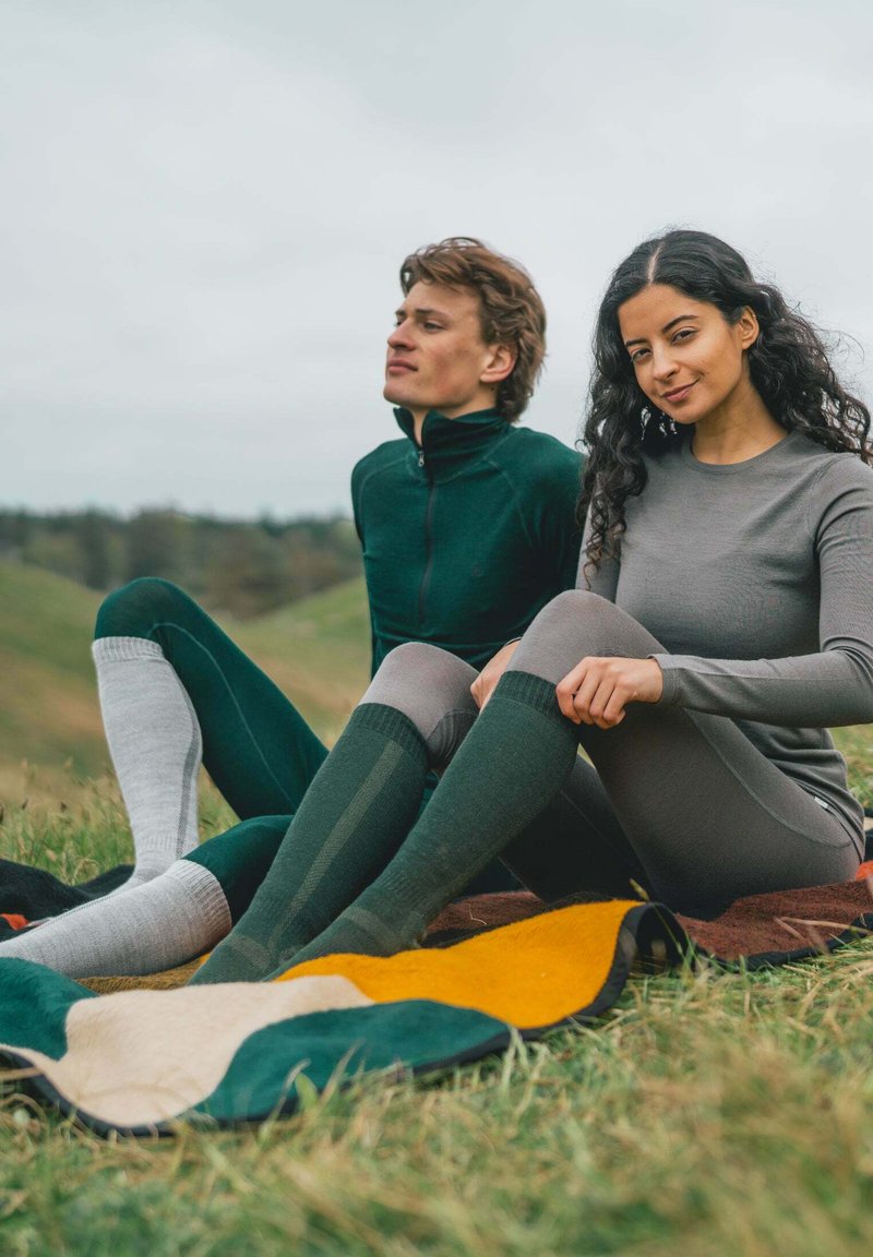 Camicie lunghe aderenti verdi e grigie con calze al ginocchio, con motivi testurizzati, sedute su una coperta colorata e a motivi sull'erba.