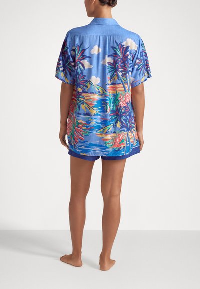 Camicia azzurra a maniche corte con stampa tropicale colorata che presenta palme e fiori, abbinata a pantaloni corti azzurri coordinati, in tessuto leggero.