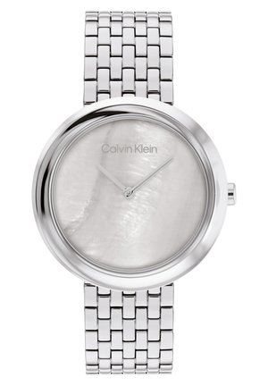 Montre-bracelet en métal argenté avec un boîtier rond, un cadran en nacre blanche, de fines aiguilles argentées, et un bracelet en acier inoxydable tressé.