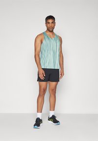 Light blue tank top with vertical stripes, black shorts, and black athletic shoes with green accents. Model stands against a plain background.