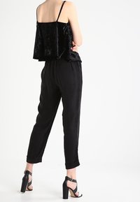 Top in velluto nero con vestibilità ampia, abbinato a pantaloni neri dal design affusolato. Tacchi trasparenti con cinturini completano l'outfit.