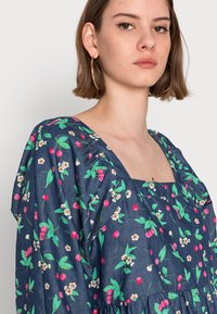 Vestido floral azul com decote quadrado, mangas curtas bufantes e cintura franzida. O tecido tem textura com padrões botânicos em rosa e verde.