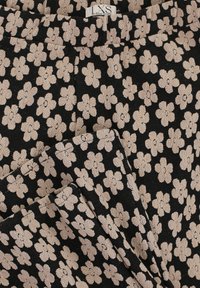 Zwarte stof met een gestructureerd bloemenpatroon in beige bloemen, met een tailleband en een gevouwen ontwerp, dat onderscheidende bloemaccenten benadrukt.