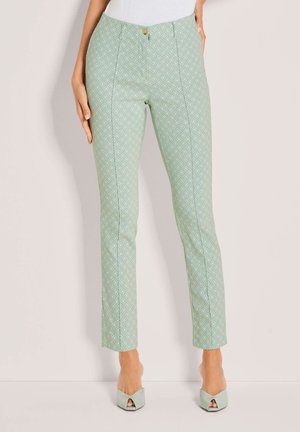 Schmal geschnittene, hellgrüne Hose mit Diamantmuster, vorne mit Knöpfen und Nahtdetails, kombiniert mit passenden, hellgrünen, offenen High-Heels.