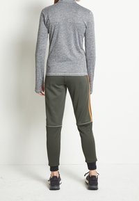 Długa szara bluzka sportowa z wysokim kołnierzem, zestawiona z oliwkowymi spodniami dresowymi z pomarańczowymi paskami po bokach i czarnymi elastycznymi mankietami.