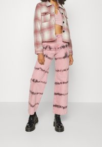 Lyserøde tie-dye vide bukser i kombination med en struktureret ternet jakke med sorte knapper og brystlomme. Sorte snørebåndsstøvler fuldender looket.