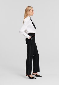 Witte lange mouwen shirt met een zwarte stropdas, gecombineerd met hoog-getailleerde zwarte broeken met zijkanten. Glimmende zwarte hakken en handschoenen.