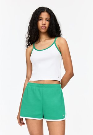 Witte cropped tanktop met groene afwerking, gecombineerd met groene shorts met witte accenten. Het materiaal lijkt zacht en casual te zijn.