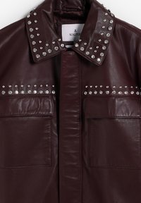 Donkerbruin leren jasje met zilveren studs op de kraag en bovenborst, voorzien van twee klepzakken en een verborgen sluiting aan de voorkant.