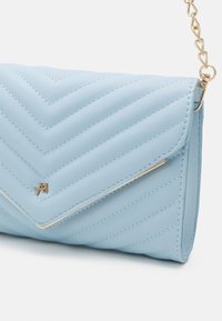 Sac en faux cuir matelassé bleu clair avec un motif chevron, une quincaillerie dorée et une bandoulière à chaîne pour le porter.