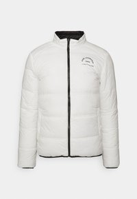 Vit puffjacka med quiltad design, svart dragkedja och hög krage. Har tryckt logotyp i svart på övre vänstra sidan.