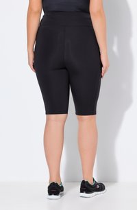 Zwarte fietsshorts met een hoge tailleband, een gladde textuur, knielengte, gecombineerd met zwarte sport schoenen met een witte zool en teal accenten.
