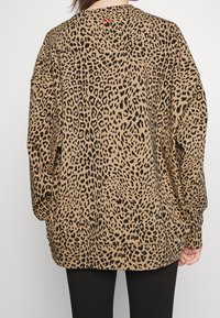 Sudadera marrón de gran tamaño con estampado de leopardo negro, con mangas largas y dobladillo redondeado. Etiqueta roja visible en el collar.