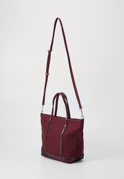 Burgundy canvas handbag with dual short handles and a detachable long strap, featuring shiny accents along the seams and base.