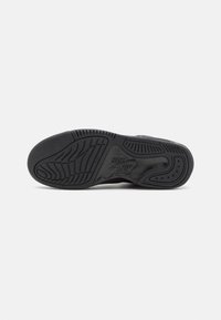Černá atletická podešev s texturovaným gripem, která obsahuje vyvýšené logo Nike Air a jasně viditelné drážky pro trakci.