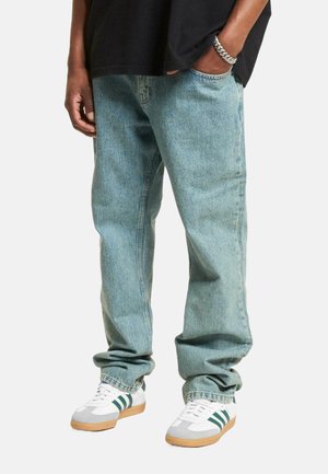 Light blue denim jeans with a loose fit, featuring five-pocket design. Paired with white sneakers with green stripes and gum sole.