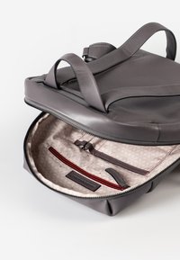 Zaino in pelle grigia con apertura con zip, caratterizzato da un interno beige a fantasie, tasca con zip rossa e numerosi scomparti organizzativi.