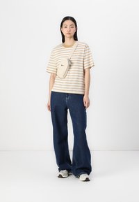 Striped beige and white oversized t-shirt, paired with dark blue wide-leg jeans. A small cream shoulder bag is worn across the body.