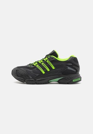 Chaussure de sport noire avec des détails vert néon, mesh respirant, semelle amortissante et soutien de talon adiPRENE de marque, vue de côté.