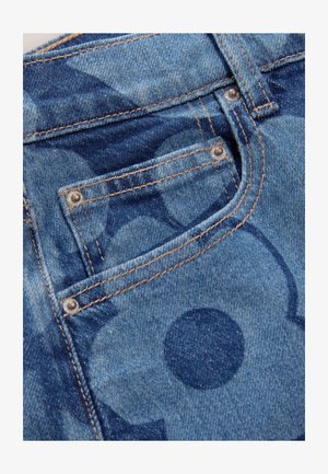 Denimstoff in Blautönen mit einem dezenten Muster aus verschiedenen Kreisen. Akzente werden durch braune Nähte und Metallnieten an den Taschen gesetzt.