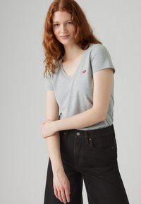 Grey cotton t-shirt with a v-neck and short sleeves, featuring a small red Levi's logo. Paired with black high-waisted pants.