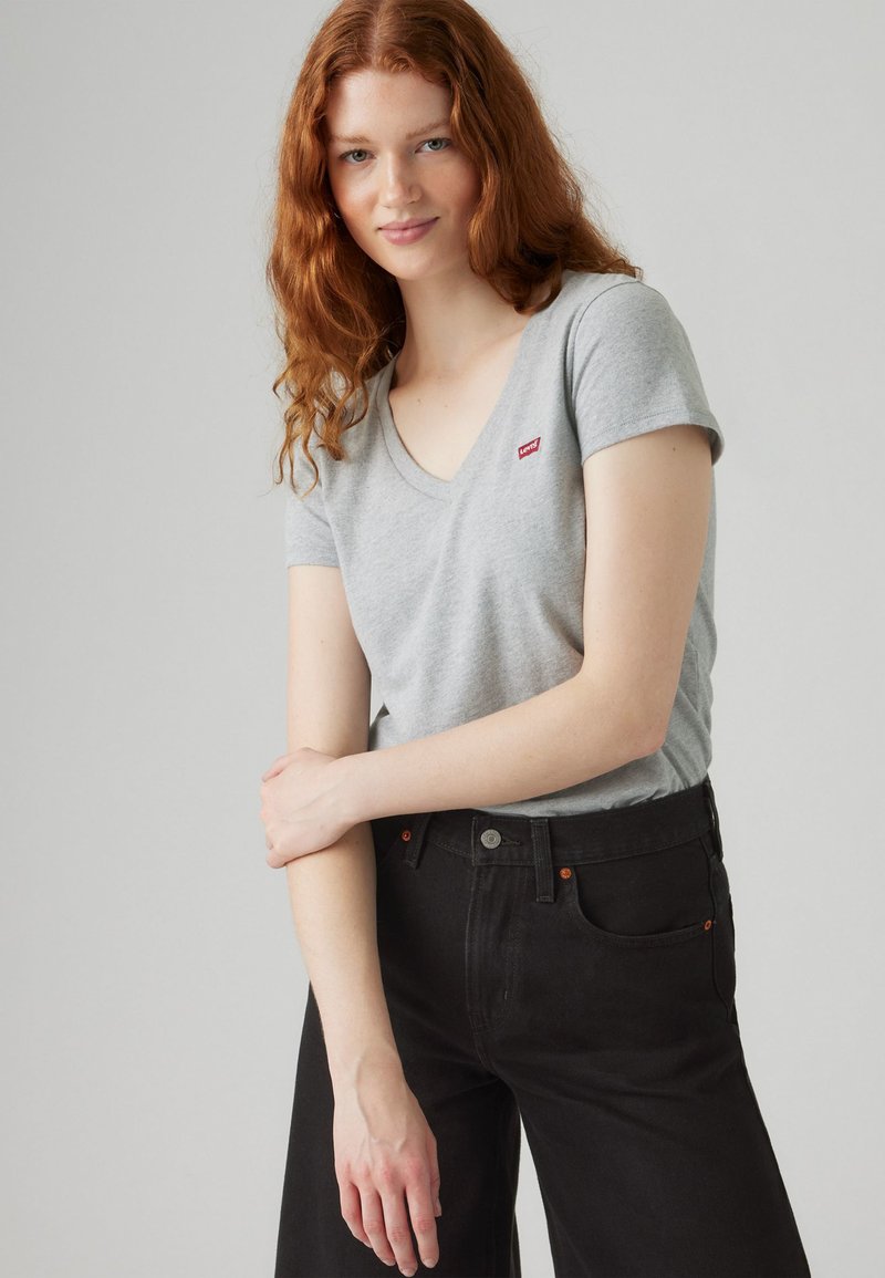 Grey cotton t-shirt with a v-neck and short sleeves, featuring a small red Levi's logo. Paired with black high-waisted pants.