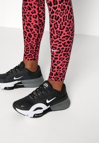 Czarne sportowe buty z białymi akcentami, połączone z legginsami w różowe wzory w panterkę. Legginsy mają gładką teksturę i dopasowany krój.