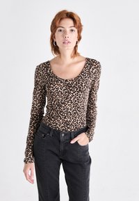 Leopardmønster langermet topp i beige og svart, med scoop hals, parret med høyhåndte svarte bukser med sidesømmer.