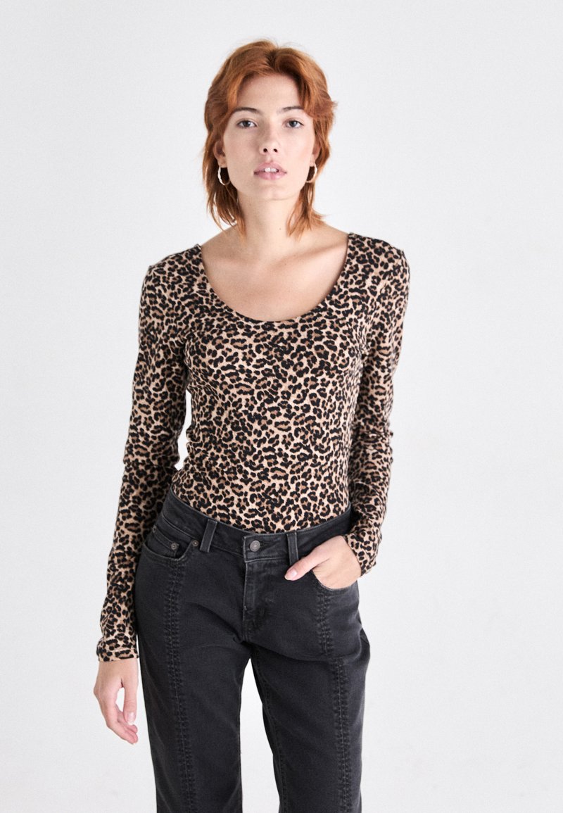 Leopardmønster langermet topp i beige og svart, med scoop hals, parret med høyhåndte svarte bukser med sidesømmer.