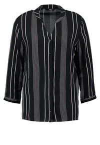 Blouse à rayures noires et blanches avec un col en V, des boutons sur le devant et des manches trois-quarts. Tissu doux avec un motif à rayures verticales.