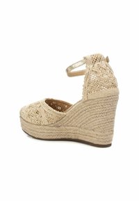 Sandalias de cuña beige con una parte superior de tejido trenzado texturizado, diseño de punta abierta, correa para el tobillo ajustable y detalles estampados en la cuña.