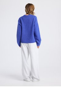 Flauschiger blauer Pullover mit lockerer Passform, rundem Ausschnitt und langen Ärmeln, kombiniert mit locker sitzenden grauen Jogginghosen für einen lässigen Look.