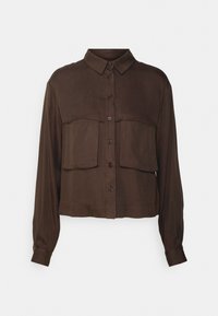 Chemise marron à boutons avec manches longues, deux poches avant et un col structuré. Matériau doux avec une texture lisse et un design court.