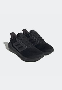 Zapatos deportivos negros con parte superior de malla transpirable, cuello acolchado y suela texturizada con acentos de diseño de tres rayas distintivas.