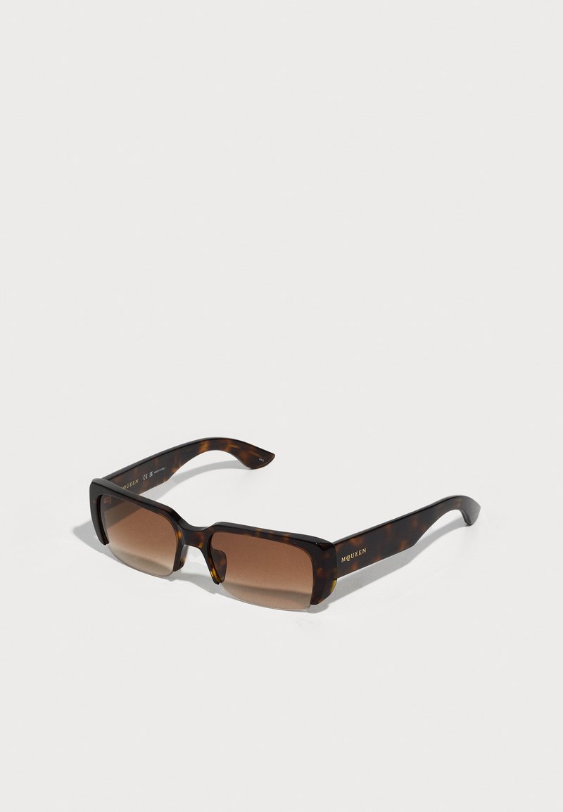 Occhiali da sole in tartaruga con lenti color marrone, forma rettangolare e montatura spessa. Presentano un sottile dettaglio del logo sul braccio.