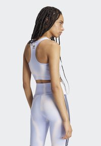 Lila športna crop majica z racerback dizajnom in podrobnostmi logotipa, v kombinaciji z usklajenimi visokimi kratkimi hlačami, ki imajo stranske črte.