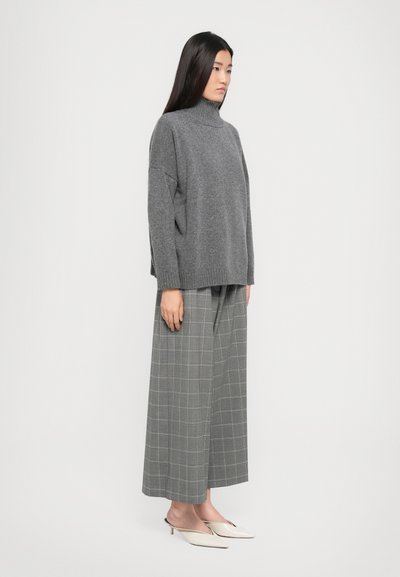 Übergroßer grauer Rollkragenpullover kombiniert mit weit geschnittenen grauen Karohosen, die feine Linien aufweisen. Das Model trägt beiger Mules.