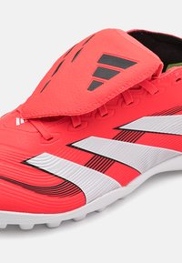 Red synthetic soccer cleat with white and black stripes. Features textured upper, rounded toe, and prominent lacing system.