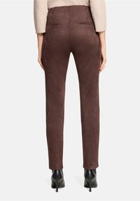 Bruine suède broek met een smalle pasvorm, voorzien van achterzakken en een gladde textuur, gecombineerd met zwarte hoge hakken.
