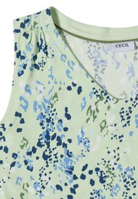 Haut sans manches vert clair avec motif floral abstrait bleu, marine et blanc et encolure ronde.