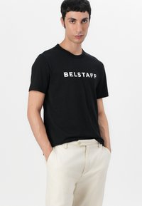 Black cotton t-shirt featuring a white "BELSTAFF" logo across the chest. Short sleeves and a classic crew neckline.