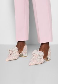 Rosa tweedklackar med spetsig tå, som har en stor rosett och texturerade detaljer, samt en låg blockklack med en kristalldetalj.