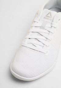 Witte sportieve schoen met een gestructureerde mesh bovenkant, platte veters en een gladde rubberen zool. Heeft het Reebok-logo op de tong en aan de zijkant.