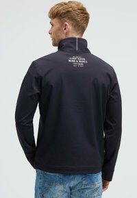 Chaqueta softshell azul marino con cuello alto, mangas largas y un logo en la espalda. Apta para actividades al aire libre.