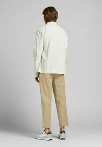 Ljust färgad oversized skjorta med en mjuk textur, kombinerad med beige något avsmalnande byxor och vita sneakers med grå detaljer.