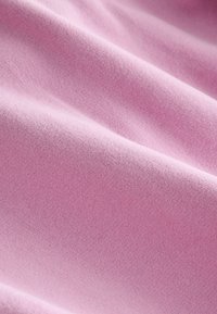 Mjuk, slät rosa tyg med mjuka veck och en fin stickad struktur, visad i närbild.