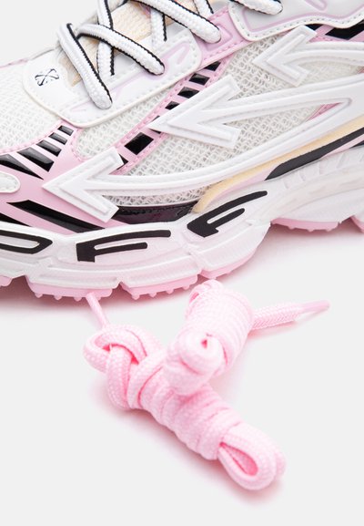 Κοντινή λήψη ροζ και λευκού αθλητικού παπουτσιού με μαύρες λεπτομέρειες, δίχτυ και χαλαρά ροζ κορδόνια πάνω σε λευκή επιφάνεια.
