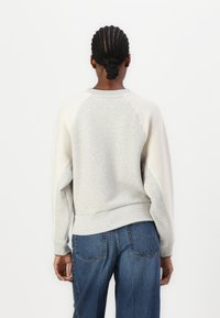 Sweatshirt gris clair avec des poignets et un ourlet côtelés ; présente des manches raglan et une texture lisse. Associé à un jean en denim bleu.